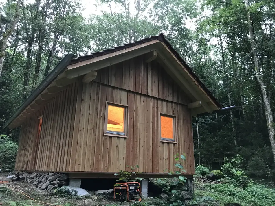 Giebelseite der Hütte mit Fenstern, aufgeständert auf Punktfundamenten